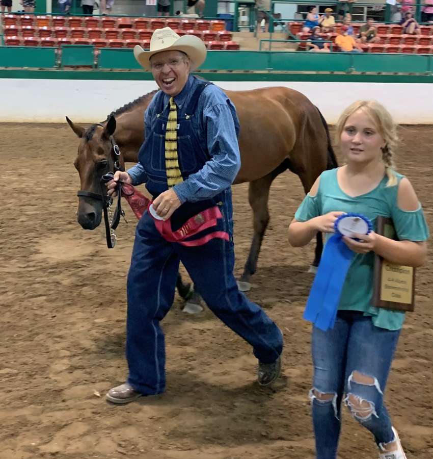 Girl holding award with man leading a horse in background