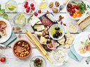 Charcuterie spread with cheeses, cured meats, olives, crackers, fruits, nuts, and drinks.