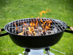 Charcoal kettle grill with lit flames and glowing coals on a green lawn