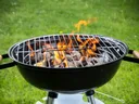 Charcoal kettle grill with lit flames and glowing coals on a green lawn