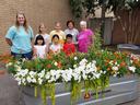 Group of seven standing behind metal planter labeled CountryLine with white and orange flowers