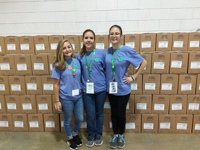 Three women in blue shirts standing in front of stacked cardboard boxes