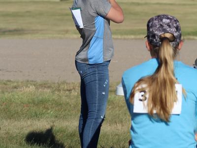 Person standing at outdoor shooting range aiming a rifle toward distant targets