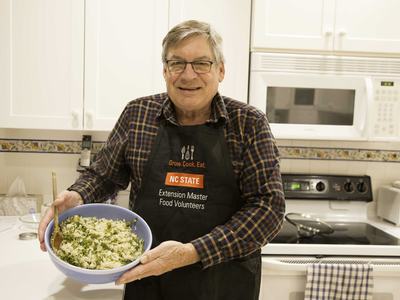Extension Master Food Volunteer in kitchen wearing apron holding meal he has helped prepare