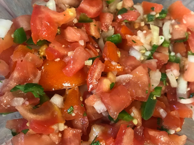 Chopped tomato salsa with diced onions, jalapeño peppers, and cilantro in a glass bowl