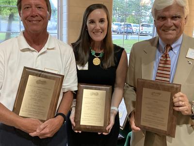 Two men and a woman looking at camera holding plaques