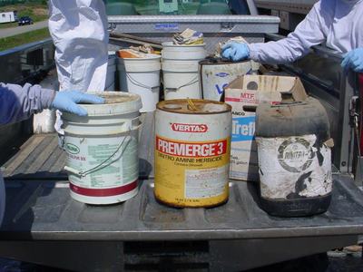 Truck bed with chemical containers including can labeled "PREMERGE 3"; gloved hands handling