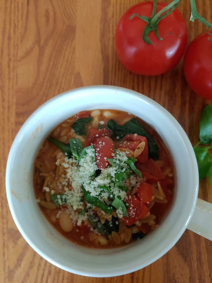 Quick Bean and Spinach Soup topped with cheese on a wooden surface with fresh vegetables surrounding the outside of the bowl