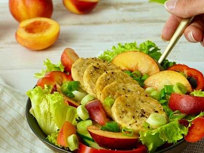 Salad with lettuce, sliced peaches, cucumber, scallions, and seasoned tofu; hand with fork