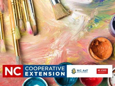 Paintbrushes and open paint jars on painted surface with "NC Cooperative Extension" banner