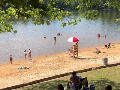 Sandy lake beach with swimmers and lifeguard seated on tower under red-and-white umbrella