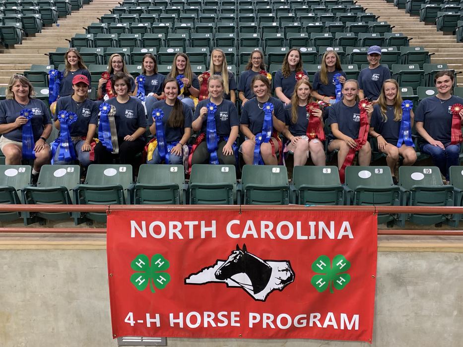 Group holding blue and red ribbons above banner "NORTH CAROLINA 4‑H HORSE PROGRAM"