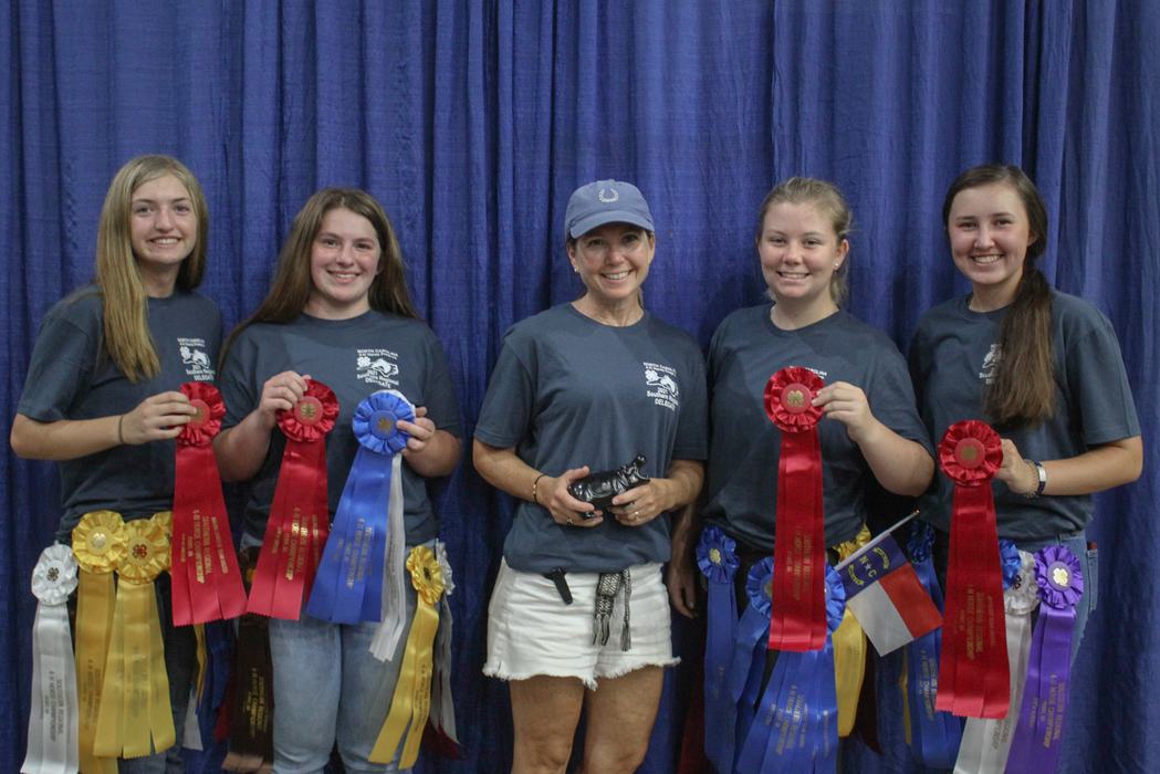 Five people standing before a blue curtain holding ribbon awards and a small black trophy