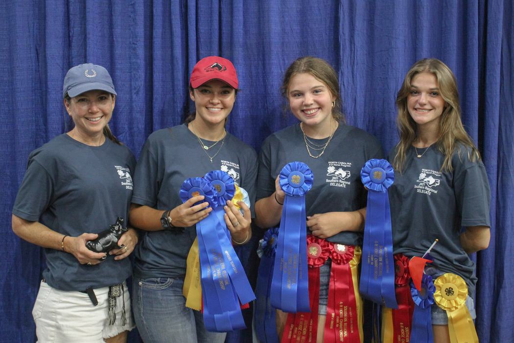Four people in matching North Carolina 4‑H shirts holding blue ribbons and awards