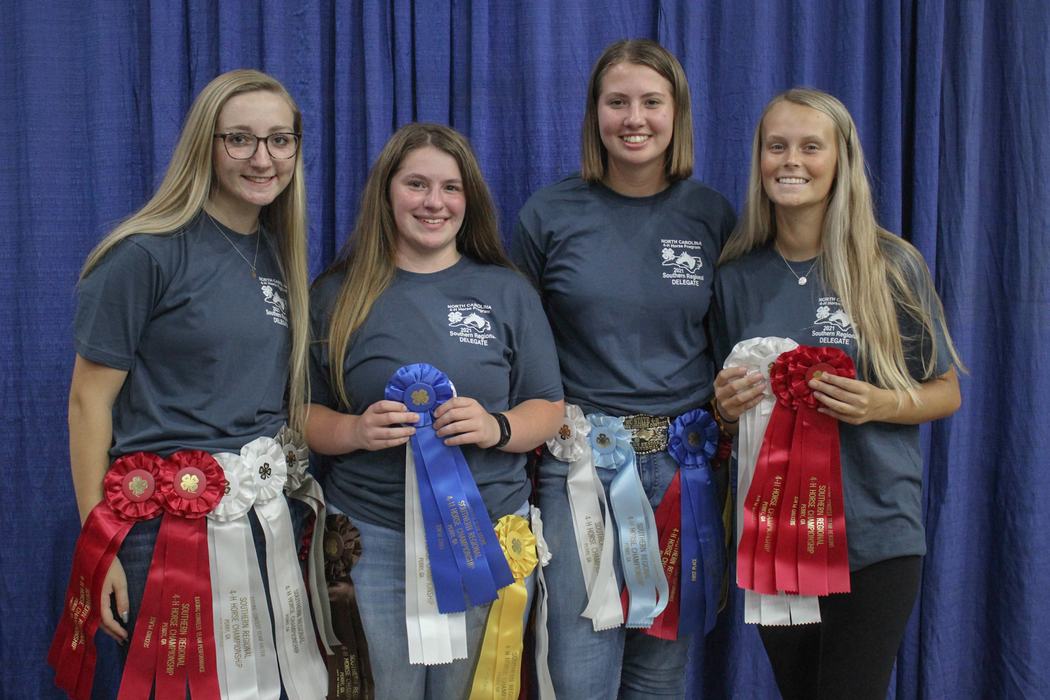 Four people in "Delegate" shirts holding multiple award ribbons against blue curtain
