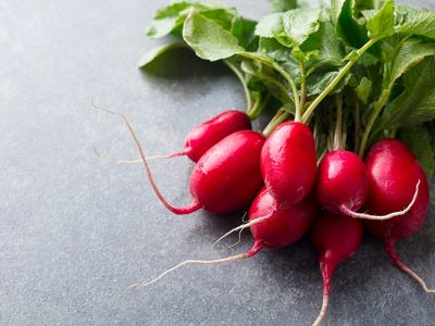 Bunch of red radishes with green leaves laid on a gray stone surface