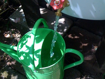 Red-handled spigot pouring water into green metal watering can.