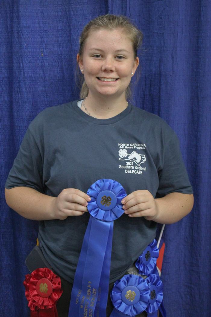 Person holding blue 4-H ribbon; shirt reads "4-H Horse Program 2021 Southern Regional Delegate"