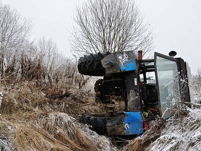 Overturned blue tractor lying on its side in a snowy, grassy field