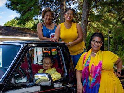 Four women posing by and inside a black pickup truck outdoors