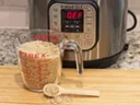 Pyrex measuring cup filled with oats, wooden scoop with oats, Instant Pot display reading "OFF"