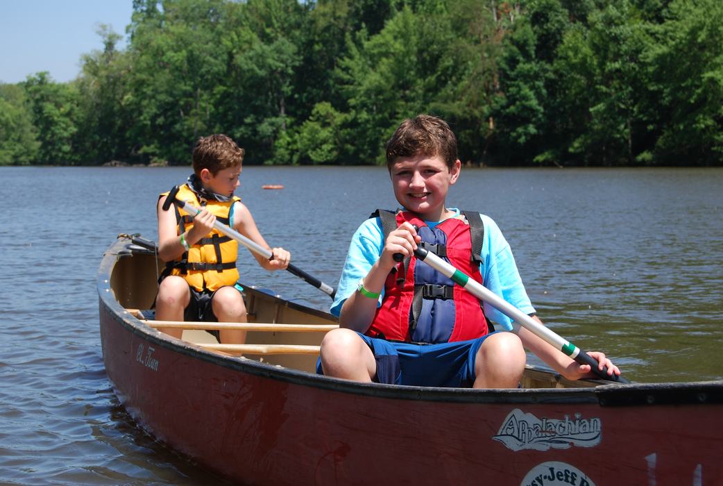 Two boys in a canoe on a lake paddling.