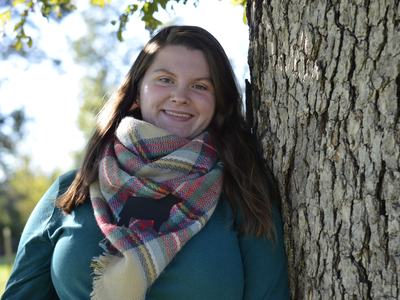 young woman wearing a scarf standing against a tree