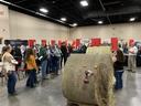 People inspecting large round hay bales at an indoor agricultural trade show