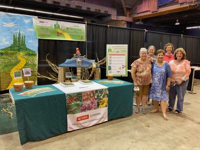 Six women standing beside an NC State Extension Master Gardener booth at an indoor fair