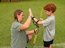 Adult instructor kneeling gives high-five to child holding a youth bow at archery range