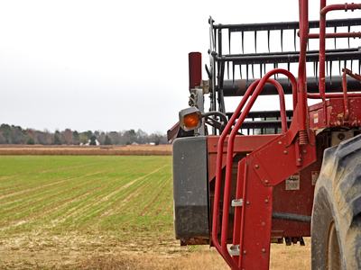 Red combine harvester front and ladder parked at edge of a green field