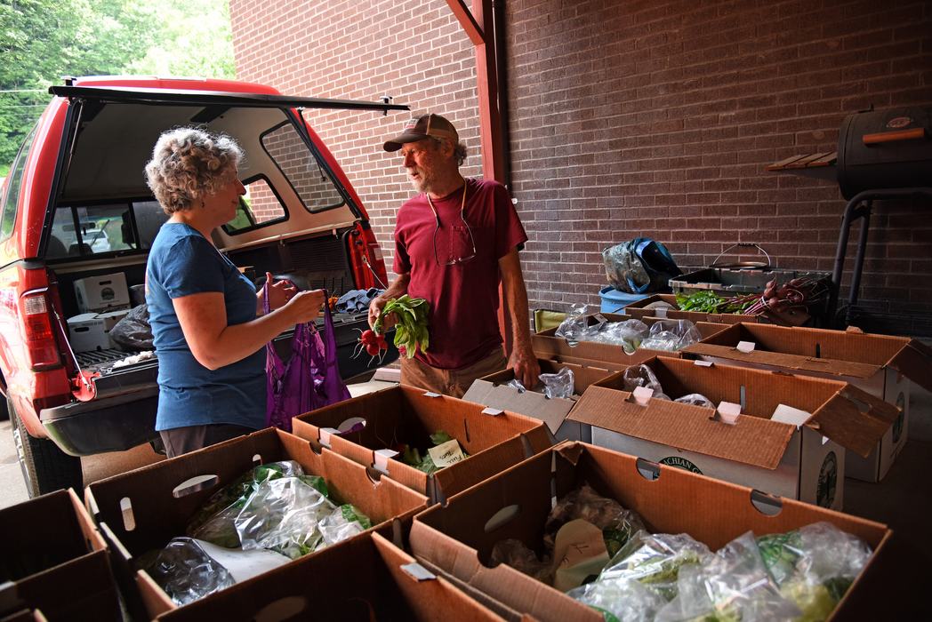 Woman taking radishes from vendor by open pickup truck and stacked boxes of produce