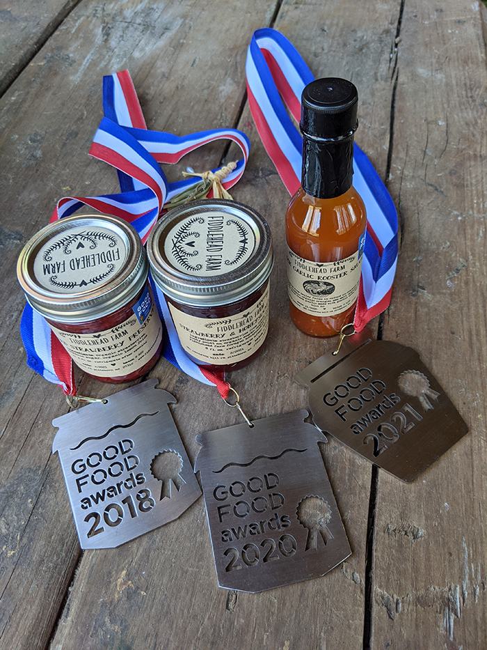 Jars and bottle with red-white-blue ribbons and medals reading "GOOD FOOD awards 2018 2020 2021"