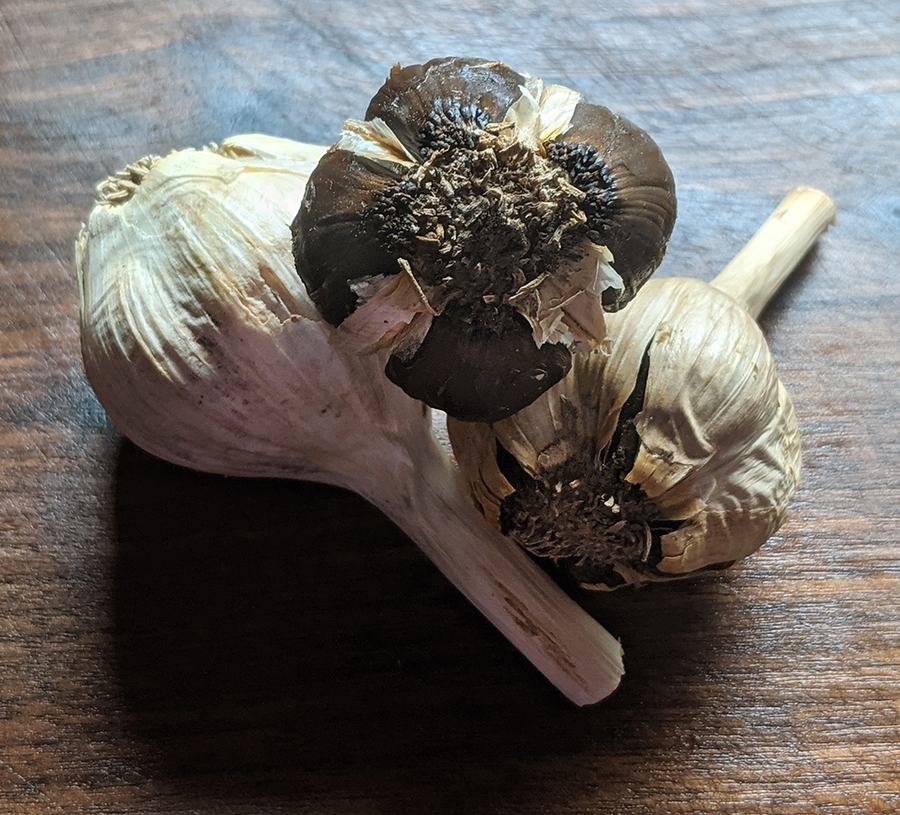 Three garlic bulbs on a wooden surface, two bulbs showing darkened root ends