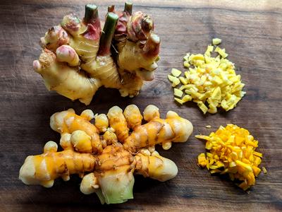 Ginger and turmeric roots on wooden cutting board with two piles of diced pieces
