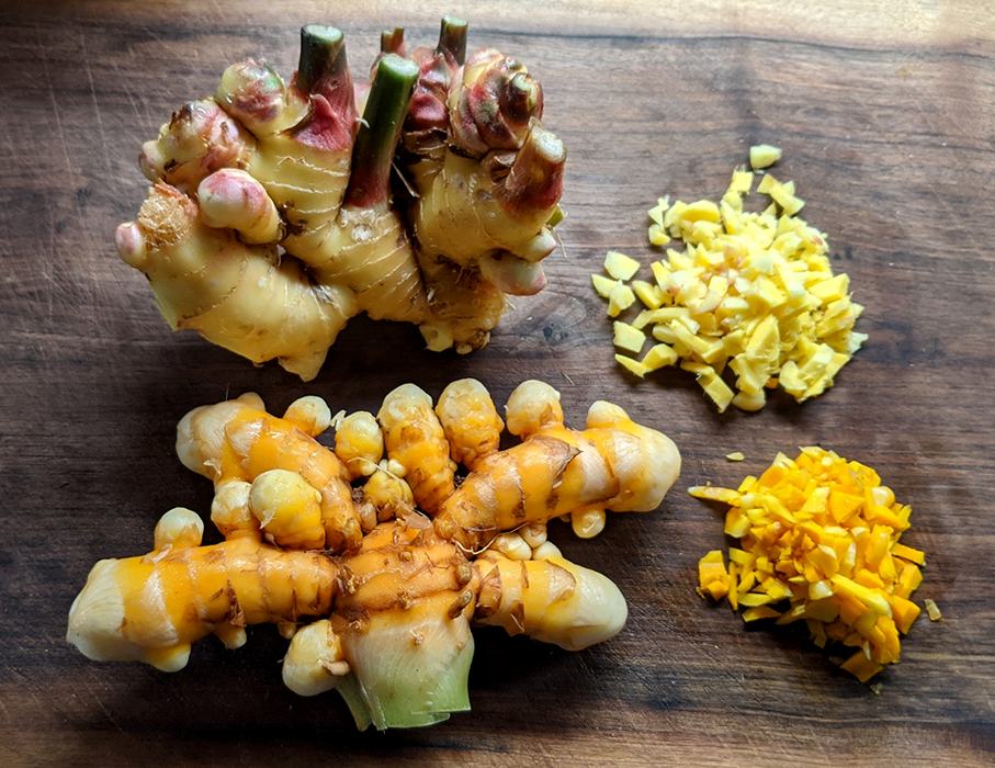 Ginger and turmeric roots on wooden cutting board with two piles of diced pieces