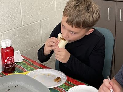 Child seated at table biting into a wrapped burrito, paper plates nearby