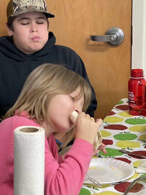 Young girl eating a burrito at a table with paper plate and red water bottle