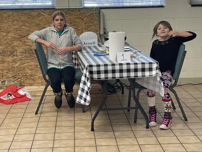 Two children seated at a checkered table with paper towel, sign "1", and paper labeled "Anna :)"