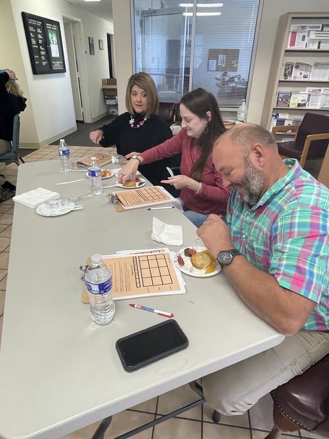 Three people seated at a table eating from plates with water bottles and clipboards