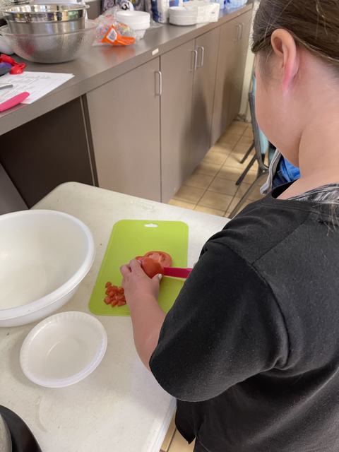 Person seen from behind chopping a tomato on a green cutting board with a pink knife