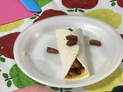 Flour tortilla wrap with cheese and filling, topped with chopped dates on paper plate