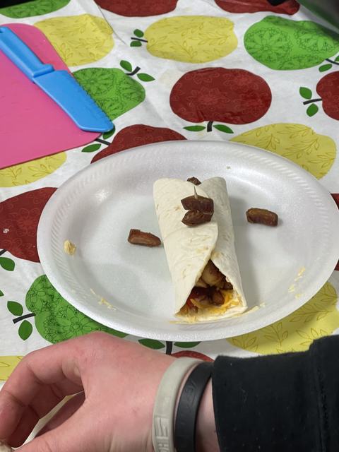 Flour tortilla wrap with cheese and filling, topped with chopped dates on paper plate