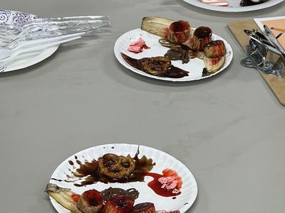 Paper plates with banana slices, pretzels, chocolate and red syrup on a table