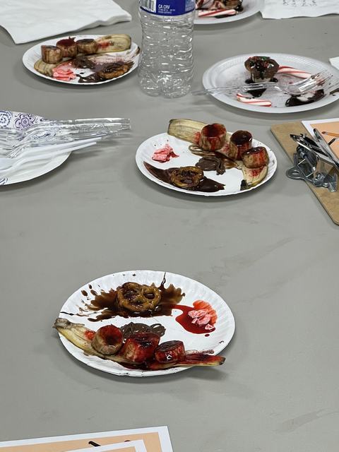 Paper plates with banana slices, pretzels, chocolate and red syrup on a table