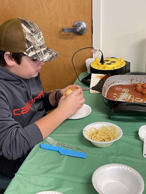 Person in Carhartt hoodie holding a roll beside a bowl of spaghetti and a pan of meatballs