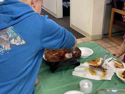 Person in blue hoodie scooping meatballs and sauce from electric skillet onto plates