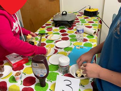 Two people assembling banana dessert at a table with a card reading "3"