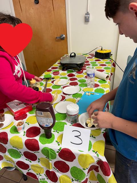 Two people assembling banana dessert at a table with a card reading "3"