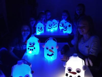 Children seated around a table displaying glowing milk-jug snowman lanterns